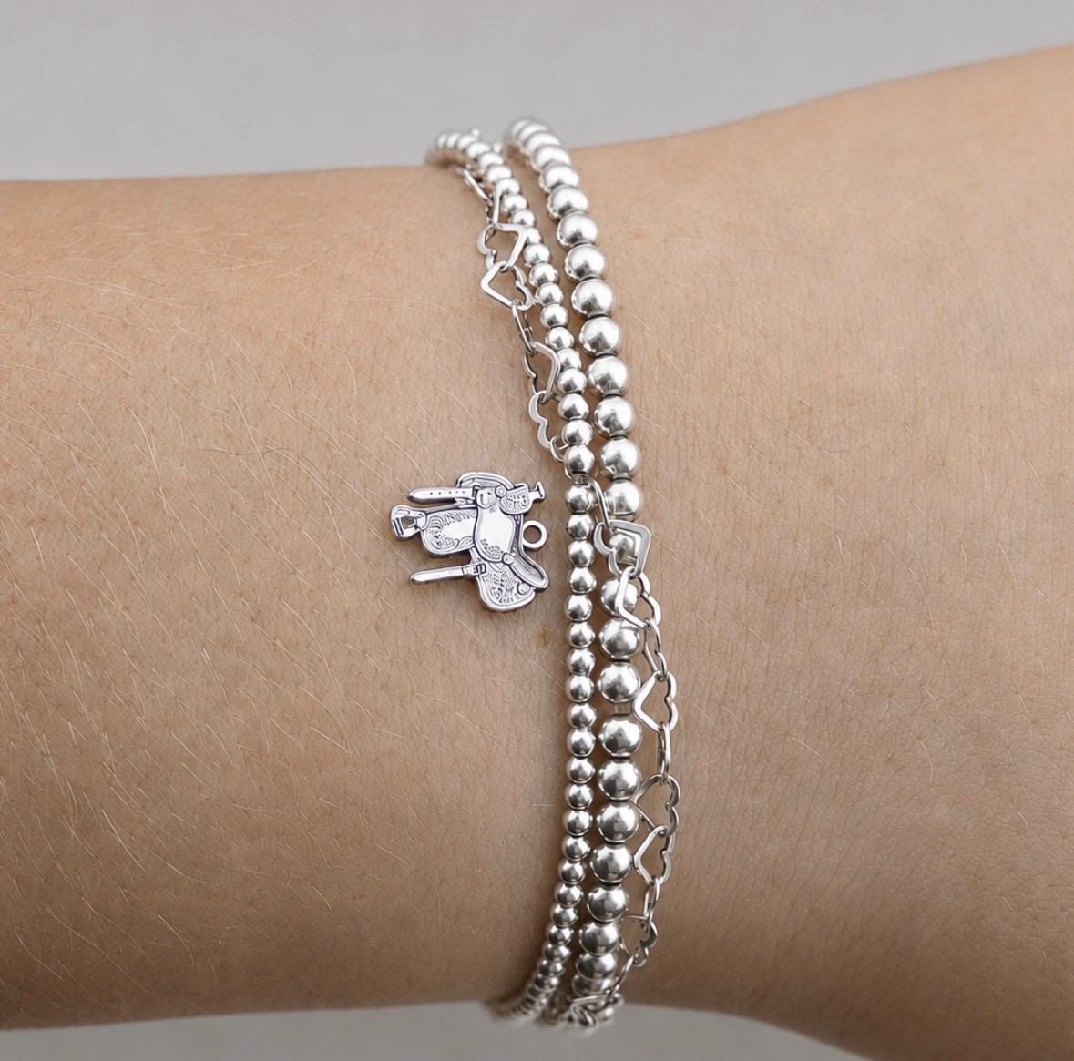 Angled view of a sterling silver western saddle charm showing detailed tooling and realistic saddle design.