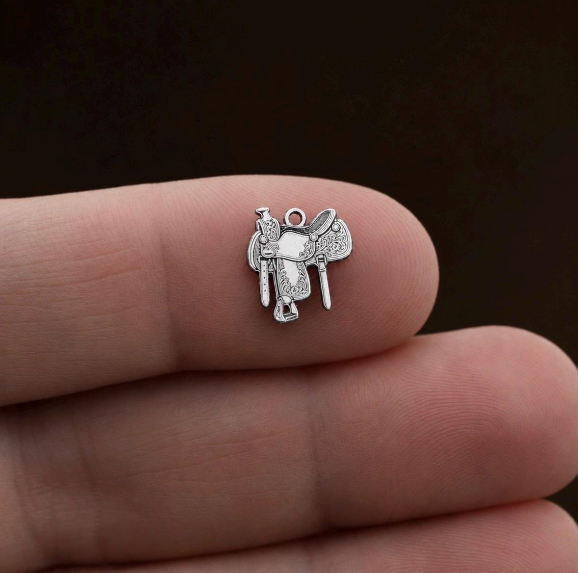 Close-up of an ornate sterling silver horse saddle charm with engraved western details and antique finish.